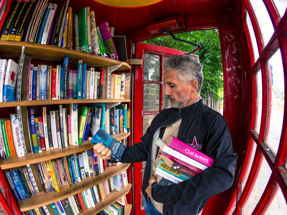 Posetilac uzima knjige iz biblioteke smeštene u preuređenoj crvenoj telefonskoj govornici na Lewisham Way u Londonu, Ujedinjeno Kraljevstvo. 
